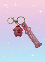 Pink keychain with a small figurine and 'Happy Day' banner on a white background