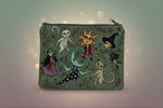Enchanted forest makeup bag featuring whimsical designs of cats, witches, and a sun on a dark green pouch.