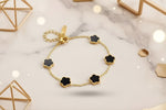 Clover charm bracelet with black flower design and gold accents on a marble background, showcasing elegance and style.