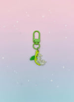 Green keychain with a leaf and floral design on a gradient pink to blue background