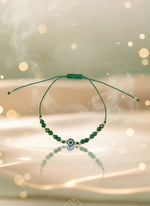 Green beaded bracelet on a cardboard holder against a light gray background