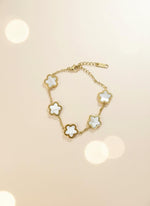 Gold bracelet with white flower-shaped charms on a light gray background