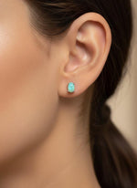 Pair of turquoise earrings on a black card with a wooden stand against a white background