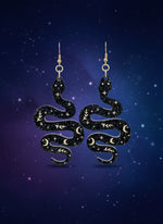Black glitter snake-shaped earrings on a wooden stand with a black background