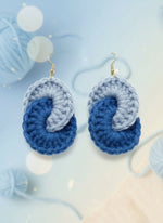 Pair of blue and gray crocheted earrings on a reflective surface.