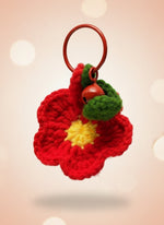 Red knitted flower with a yellow center and green leaves on a wooden stick against a plain background