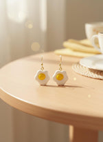 Egg-shaped earrings on a black card with a wooden stand