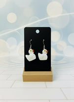 White duck-shaped earrings on a black card with a wooden stand against a white background