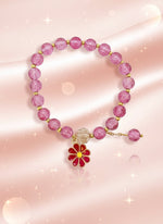 Pink beaded bracelet with a floral charm on a cardboard stand against a white background