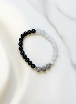 Two beaded bracelets on a white background with a brown cardboard holder.