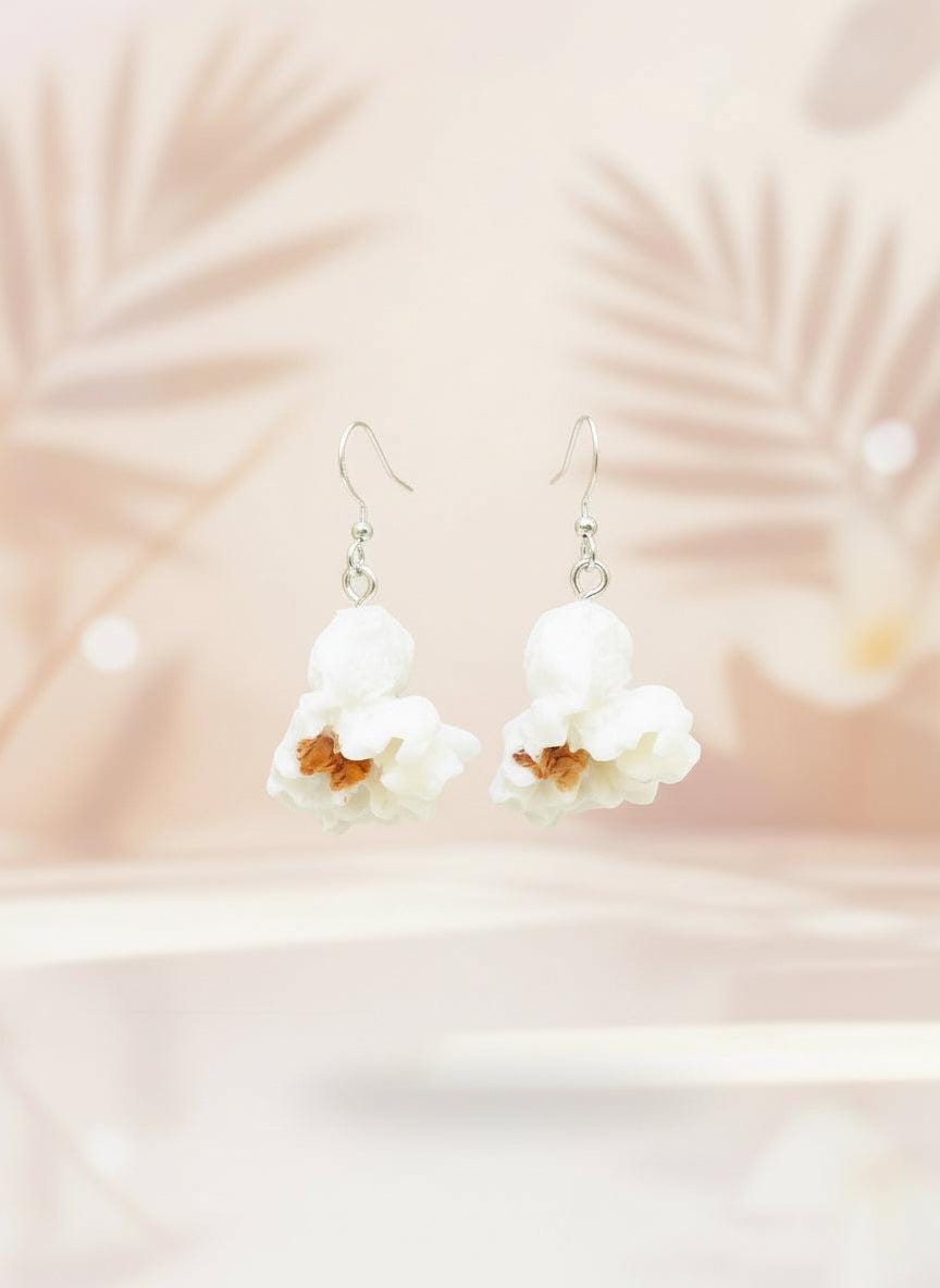 White floral earrings on a black card with a wooden stand