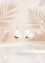 White floral earrings on a black card with a wooden stand