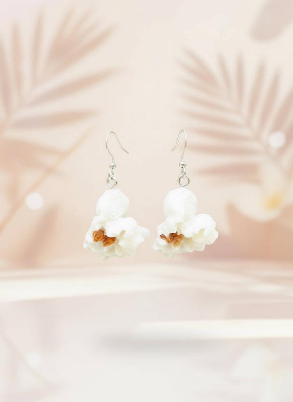 White floral earrings on a black card with a wooden stand