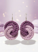 Pair of purple and gray crocheted earrings on a reflective surface.