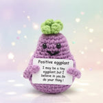 Positive Eggplant Crochet Doll with Wooden Stand holding a sign that reads 'I believe in you. Go do your thing!'. Cute desk buddy.